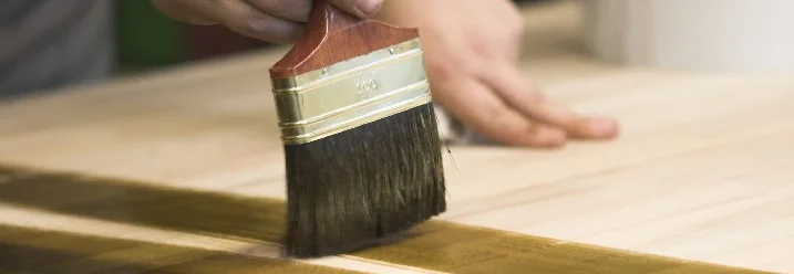 Person beizt Holz mit Pinsel